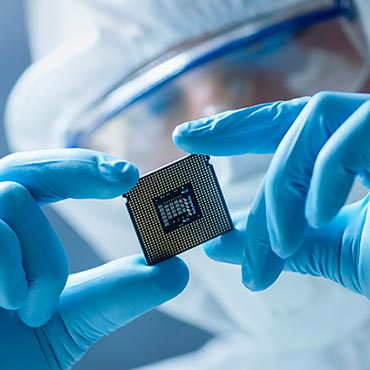 Electronics manufacturing worker in a clean suit inspecting an electronic chip